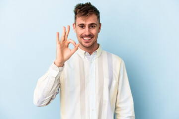 Young caucasian man isolated on blue background cheerful and confident showing ok gesture.