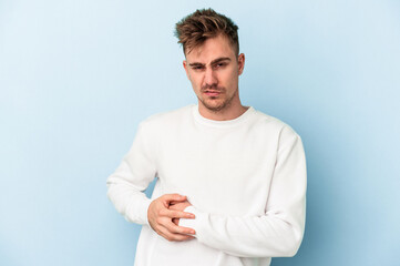 Young caucasian man isolated on blue background having a liver pain, stomach ache.