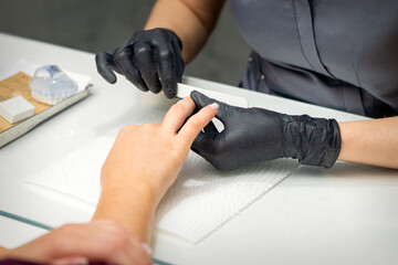 Woman receiving a manicure with nail file by a manicure master in a nail salon