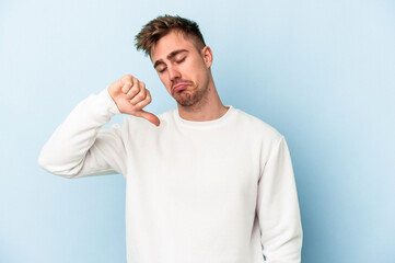 Young caucasian man isolated on blue background showing a dislike gesture, thumbs down....