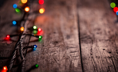 christmas garland of colorful light bulbs on an dark old weathered vintage table or wooden brown board. Christmas decoration, New Years Eve. Selective focus, bokeh, space for text.