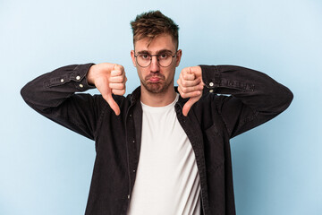 Young caucasian man isolated on blue background showing a dislike gesture, thumbs down. Disagreement concept.