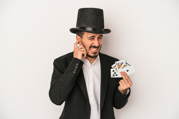 Young magician man holding a magic card isolated on white background covering ears with hands.