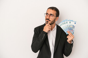 Young caucasian business man holding banknotes isolated on white background looking sideways with doubtful and skeptical expression.