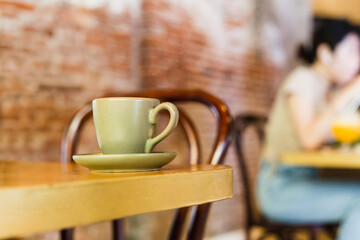 Green clay cup with coffee on wooden table in cafe.