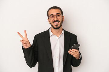 Young business man holding a mobile phone isolated on white background joyful and carefree showing a peace symbol with fingers.