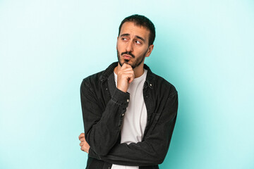 Young caucasian man isolated on blue background relaxed thinking about something looking at a copy space.