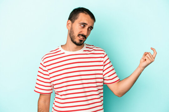 Young caucasian man isolated on blue background pointing with finger at you as if inviting come closer.