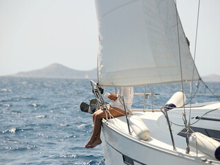 A woman reads a book on the bow of a sailing yacht. Luxurious life on a white yacht. Psychological relaxation and outdoor recreation. Yachting availability for people of average income.