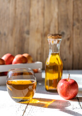 Apple juice in the glass with apples, bottle on the wooden table and light grey background
