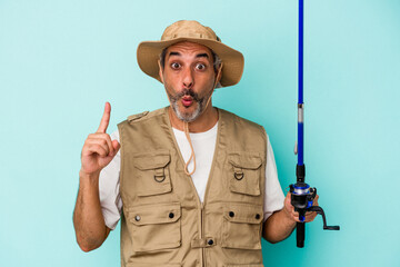 Middle age caucasian fisherman holding rod isolated on blue background  having some great idea, concept of creativity.