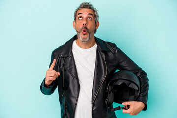 Middle age biker caucasian man holding helmet isolated on blue background  pointing upside with...