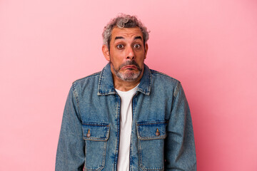 Middle age caucasian man isolated on pink background  shrugs shoulders and open eyes confused.