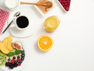cup of black coffee, a plate of oatmeal and fruit, honey and a glass of milk on a white table