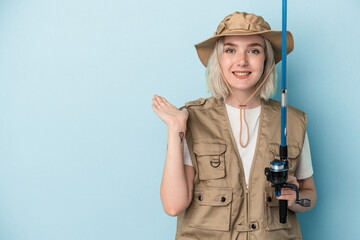 Young caucasian fisherwoman holding a rod isolated on blue background showing a copy space on a palm and holding another hand on waist.