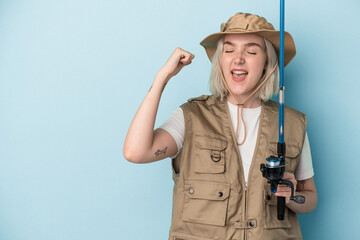 Young caucasian fisherwoman holding a rod isolated on blue background raising fist after a victory, winner concept.