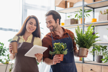 Young sellers holding plants and digital tablet in flower shop