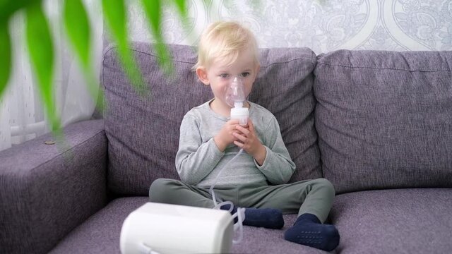 Cute little blond boy does inhalation at home.