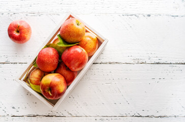 Apples in a white wooden box on the white wooden background with copy space, top view