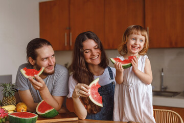 A family in the kitchen cuting and eating the watermelon at home. Happy family of mother, father...