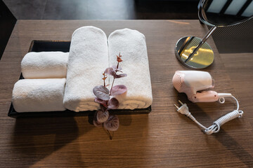 Towels white softness cotton clean textile neatly folded clothes with pink hair dryer and mirror on wooden table.