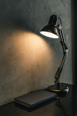 Retro black metal desk lamp or flexible table lamp light bulb on the black table and blue book with...