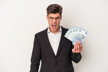 Young business caucasian man holding banknotes isolated on white background screaming very angry and aggressive.