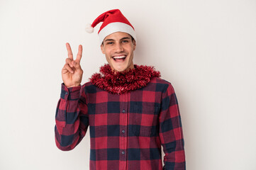 Young caucasian man celebrating Christmas isolated on white background joyful and carefree showing a peace symbol with fingers.