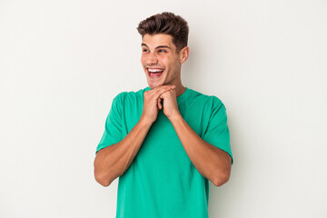 Young caucasian man isolated on white background keeps hands under chin, is looking happily aside.