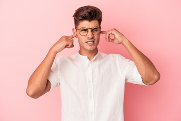 Young caucasian man isolated on pink background covering ears with fingers, stressed and desperate by a loudly ambient.