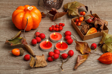 Lit candles, berries, decorative pumpkin and leaves on the table. Autumn crafts made of leaves, vegetables, acorns and other items