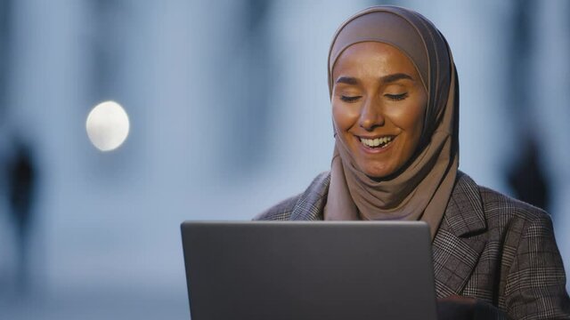 Portrait arabic islamic muslim business woman girl international student speaks video chat conference using laptop talking in web camera sitting in evening night on street in city remote conversation