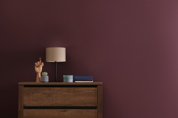 Books, decor and lamp on chest of drawers near brown wall indoors, space for text. Interior design