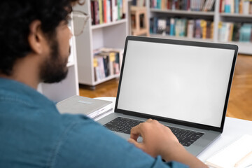 Indian teen male student working with laptop white screen mockup at library