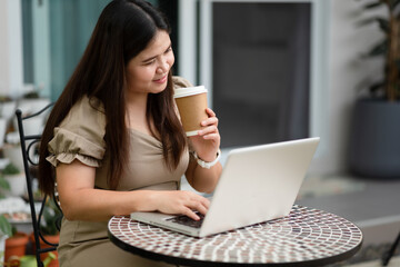 Fototapeta premium Asian woman is using her laptop to check email and work via the internet with a coffee next to her ,Working from home concept.