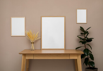 Empty frames, wooden table and plant near pale rose wall. Mockup for design