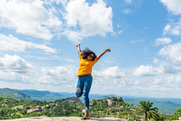 young black lady jumps with excitement, in front of a beautiful landscape