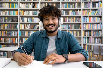 Portrait of smiling Indian student in headset looking at camera at library desk