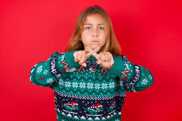 brunette kid girl in knitted sweater christmas over red background has rejection angry expression...