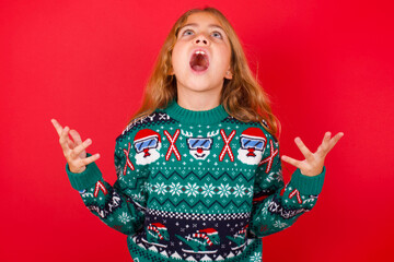 brunette kid girl in knitted sweater Christmas over red background  crying and screaming. Human emotions, facial expression concept. Screaming, hate, rage.