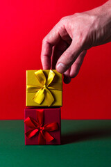 A man's hand holds a gold gift box with a bow. Two gifts on a Christmas background from the front view.