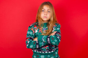 Picture of angry brunette kid girl in knitted sweater christmas over red background looking camera.
