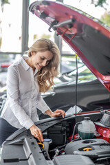 Joyful woman looking into open hood of car