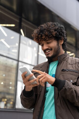 Happy smiling young Indian man walking city street using mobile phone 