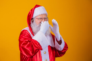 Santa Claus isolated against yellow background, smelling something stinky and disgusting, an unbearable smell, holding his breath with fingers in his nose. Bad smells concept. - obrazy, fototapety, plakaty
