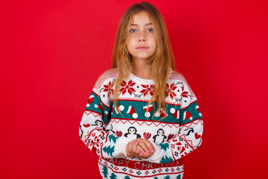Photo of cheerful confident brunette kid girl in knitted sweater christmas over red background arms together