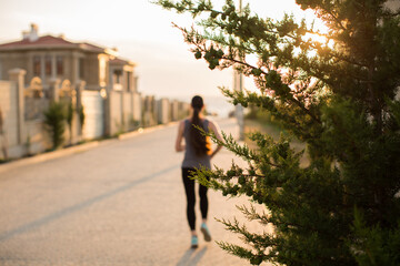 Young sporty woman running in the city at sunset. Rear view sporty girl working on the waterfront