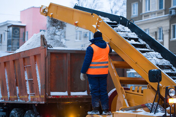 Snow cleaning tractor (snow-removal machine) loading pile of snow on a dump truck. Isolate. Snow plow outdoors cleaning street city after blizzard or snowfall