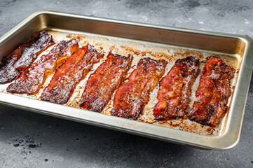 Strips of fried bacon in baking dish. Gray background. Top view