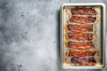 Strips of fried bacon in baking dish. Gray background. Top view. Copy space